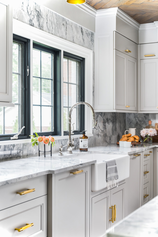 Example of a mid-sized transitional medium tone wood floor and brown floor enclosed kitchen design in Chicago with a farmhouse sink, recessed-panel cabinets, gray cabinets, quartzite countertops, gray backsplash, stone slab backsplash, paneled appliances, an island and gray countertops