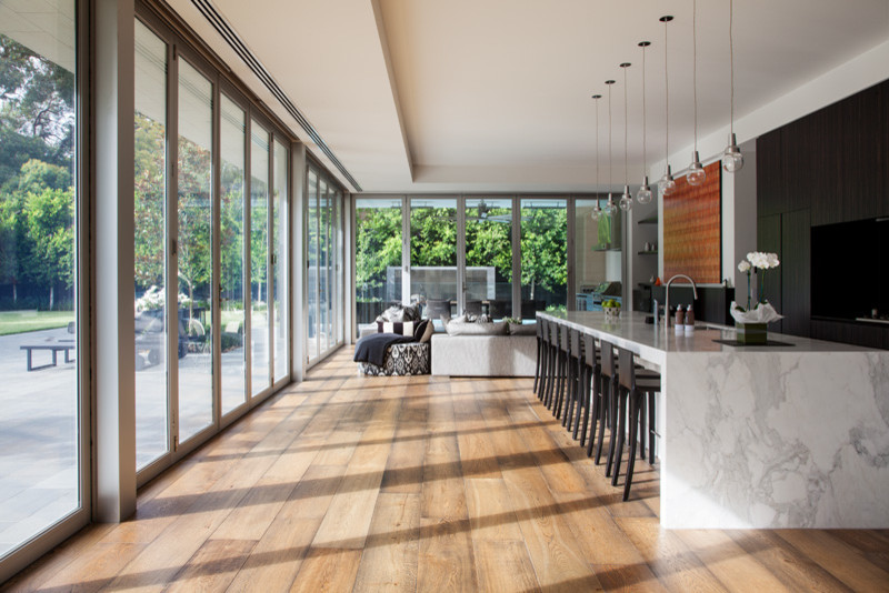 Large contemporary single-wall open plan kitchen in Melbourne with recessed-panel cabinets, dark wood cabinets, marble benchtops, with island, panelled appliances, a double-bowl sink, medium hardwood floors and brown floor.