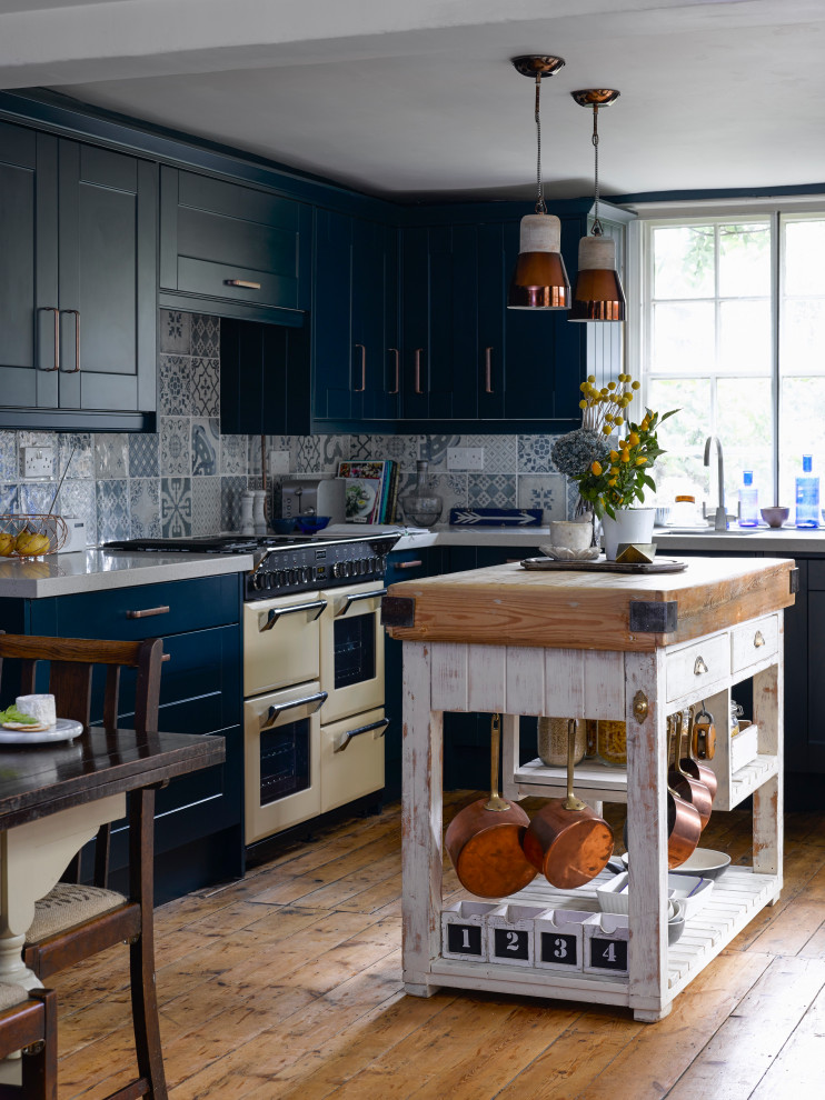Стильный дизайн: угловая кухня: освещение в стиле кантри с обеденным столом, фасадами в стиле шейкер, столешницей из акрилового камня, синим фартуком, фартуком из керамической плитки, паркетным полом среднего тона, белой столешницей, врезной мойкой, синими фасадами, цветной техникой, островом и коричневым полом - последний тренд