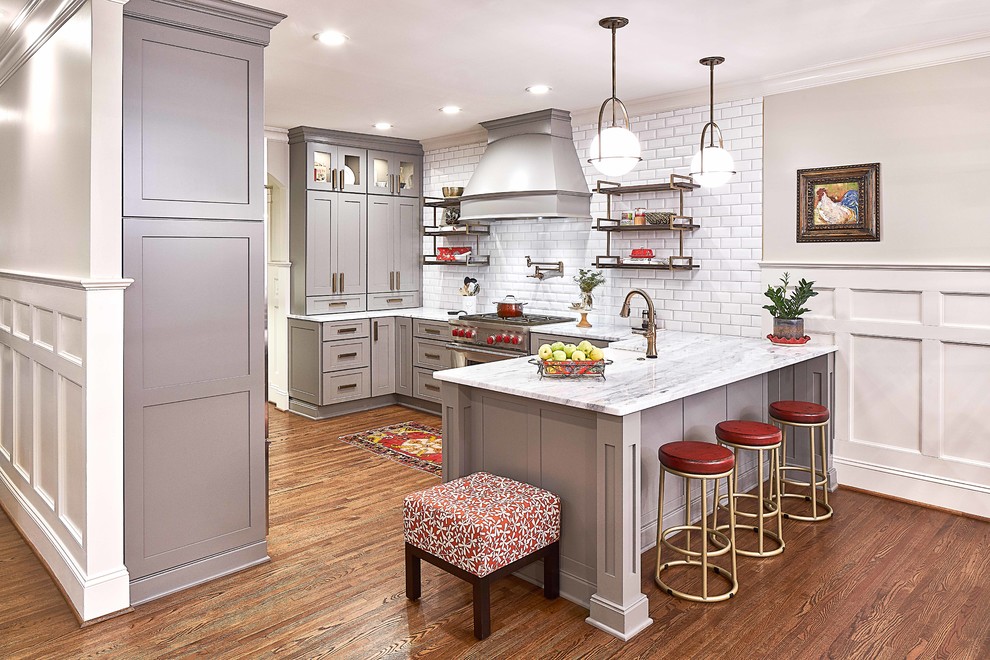 Mid-sized transitional u-shaped eat-in kitchen with a farmhouse sink, shaker cabinets, grey cabinets, marble benchtops, white splashback, subway tile splashback, stainless steel appliances, medium hardwood floors, a peninsula, brown floor and white benchtop.