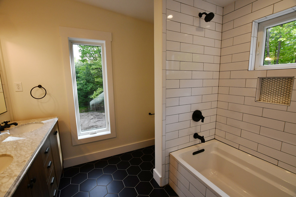 This is an example of a mid-sized midcentury master bathroom in New York with flat-panel cabinets, brown cabinets, a drop-in tub, an alcove shower, a one-piece toilet, white tile, subway tile, grey walls, porcelain floors, a drop-in sink, marble benchtops, black floor, a hinged shower door and white benchtops.