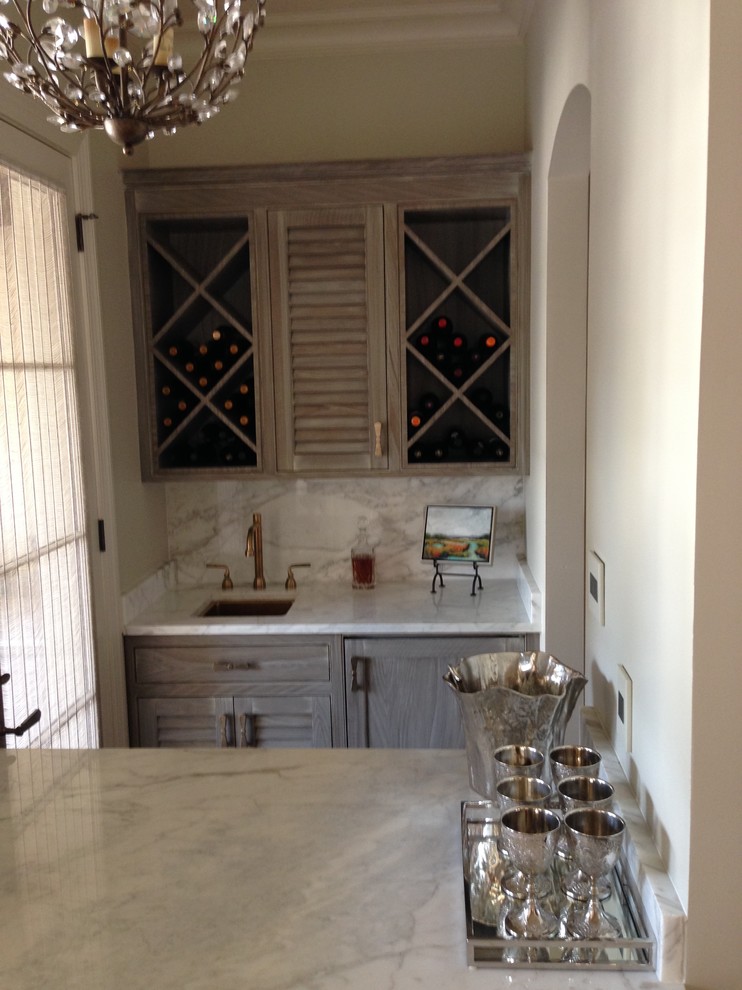 Small transitional galley wet bar in New Orleans with shaker cabinets, an undermount sink, medium wood cabinets, marble benchtops, grey splashback, marble splashback and grey benchtop.