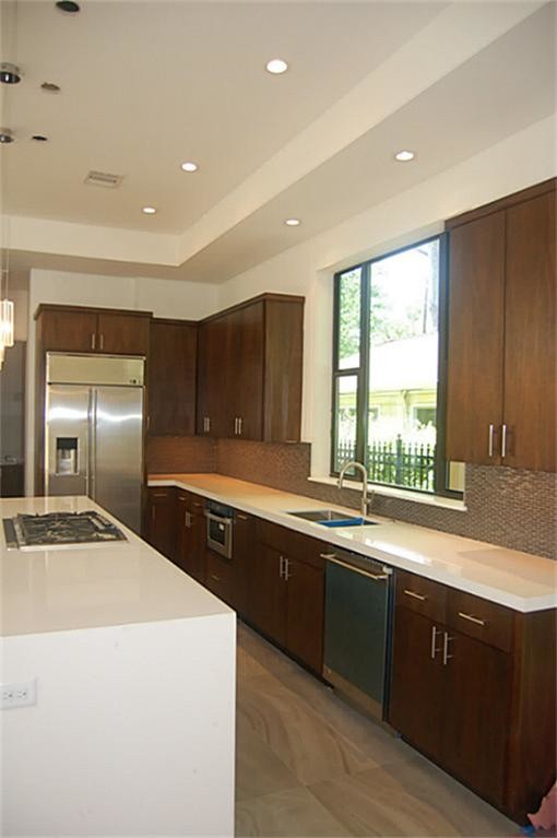 This is an example of a large contemporary l-shaped open plan kitchen in Houston with an undermount sink, flat-panel cabinets, dark wood cabinets, solid surface benchtops, brown splashback, mosaic tile splashback, stainless steel appliances, porcelain floors and with island.