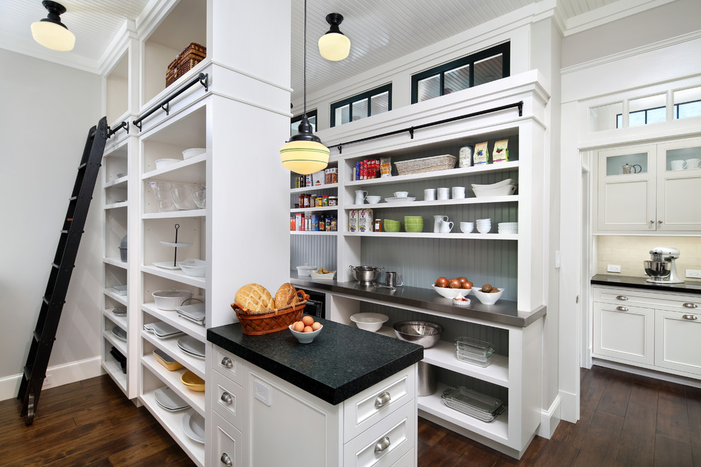 Photo of a large traditional l-shaped kitchen pantry in San Francisco with white cabinets, dark hardwood floors, a farmhouse sink, recessed-panel cabinets, granite benchtops, white splashback, subway tile splashback, black appliances, with island and brown floor.