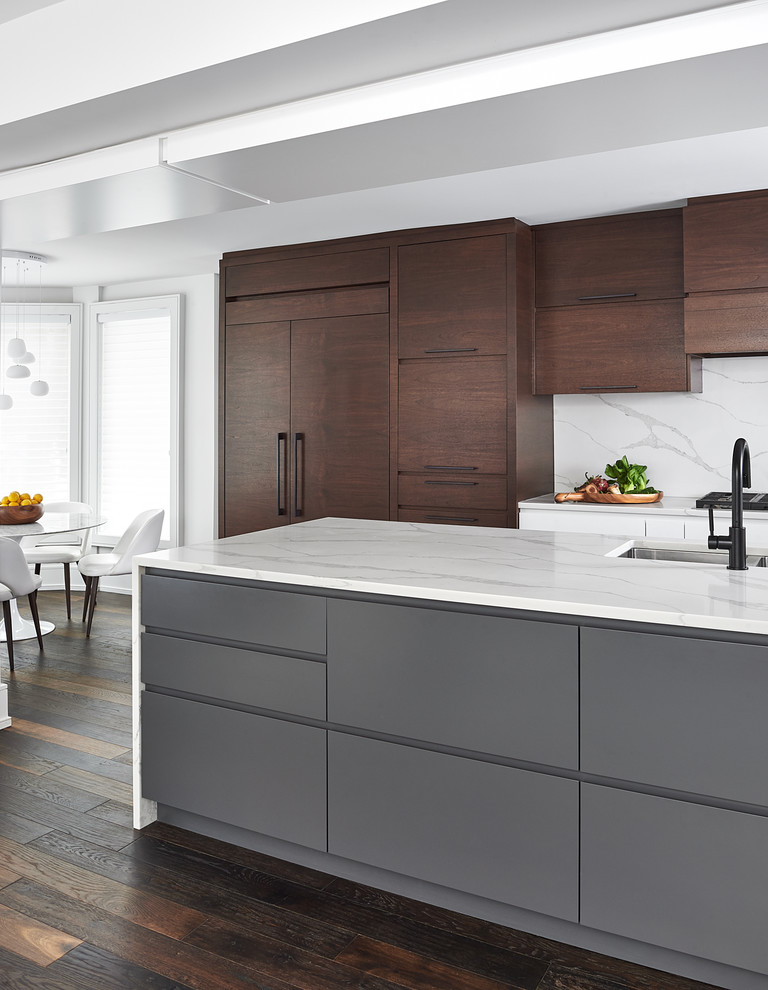 This is an example of an expansive contemporary galley open plan kitchen in Toronto with an undermount sink, flat-panel cabinets, dark wood cabinets, quartz benchtops, white splashback, stone slab splashback, panelled appliances, dark hardwood floors, with island and white benchtop.