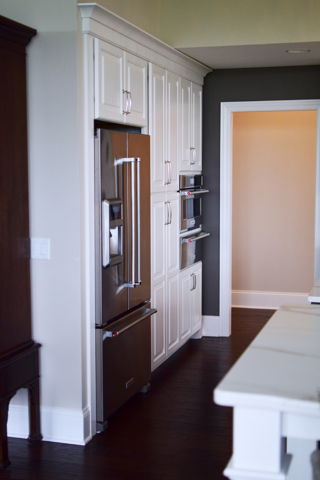 Example of a large transitional l-shaped medium tone wood floor and brown floor eat-in kitchen design with a farmhouse sink, shaker cabinets, white cabinets, quartz countertops, white backsplash, marble backsplash, stainless steel appliances and two islands