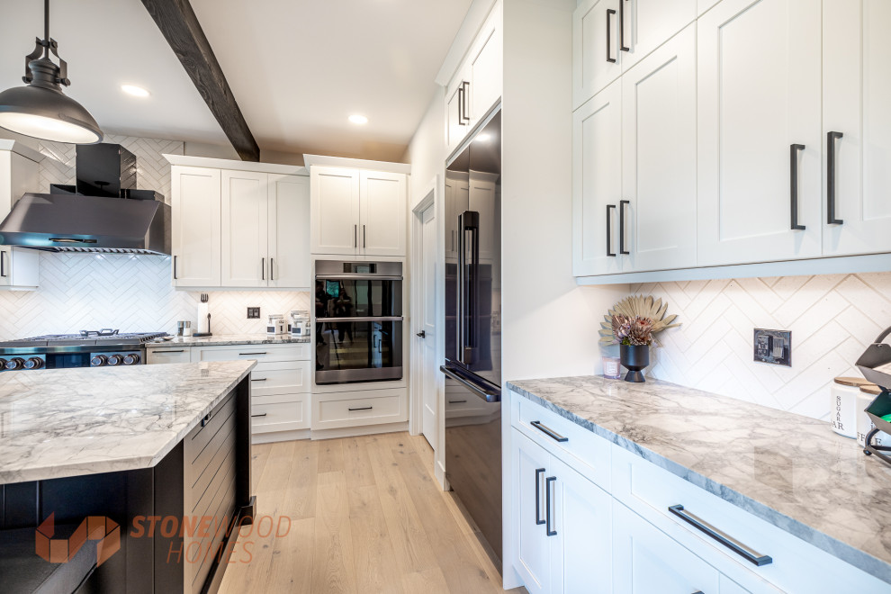 Photo of a large rural l-shaped open plan kitchen in Edmonton with a belfast sink, shaker cabinets, white cabinets, composite countertops, white splashback, ceramic splashback, stainless steel appliances, light hardwood flooring, an island, brown floors, white worktops and exposed beams.