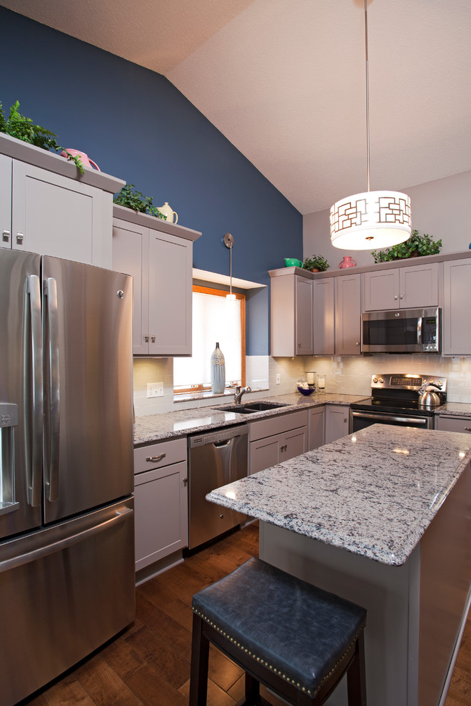 Enclosed kitchen - mid-sized transitional l-shaped medium tone wood floor enclosed kitchen idea in Minneapolis with an undermount sink, recessed-panel cabinets, gray cabinets, quartz countertops, white backsplash, porcelain backsplash, stainless steel appliances, blue walls and an island