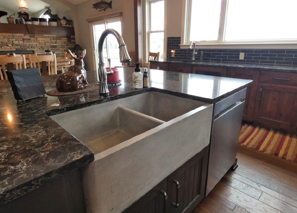 Photo of a country kitchen in Grand Rapids with a farmhouse sink, recessed-panel cabinets, dark wood cabinets, quartz benchtops, black splashback, travertine splashback, stainless steel appliances, with island and brown benchtop.