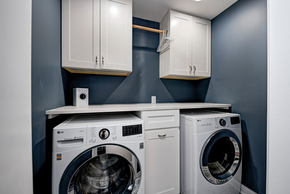 Modelo de cuarto de lavado contemporáneo con armarios estilo shaker, puertas de armario blancas, paredes azules, lavadora y secadora juntas y encimeras blancas