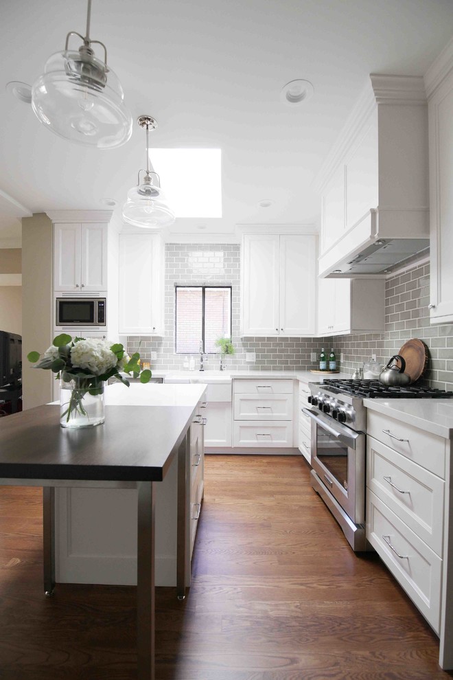 This is an example of a mid-sized arts and crafts eat-in kitchen in Salt Lake City with a farmhouse sink, shaker cabinets, white cabinets, grey splashback, stainless steel appliances, medium hardwood floors, with island and white benchtop.