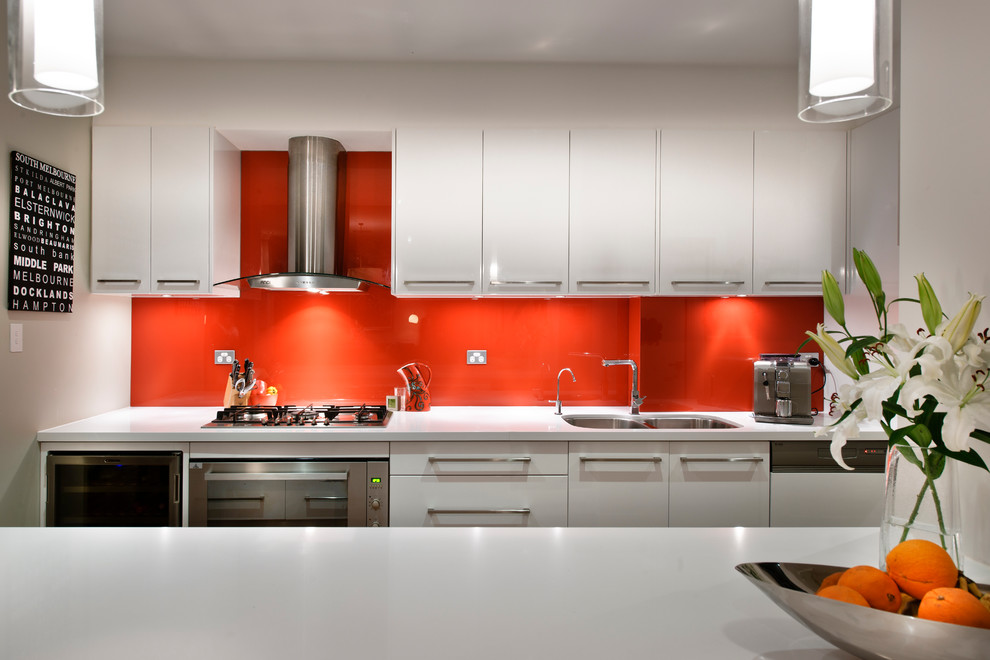 Photo of a contemporary galley open plan kitchen in Perth with a double-bowl sink, flat-panel cabinets, white cabinets, red splashback, stainless steel appliances and with island.
