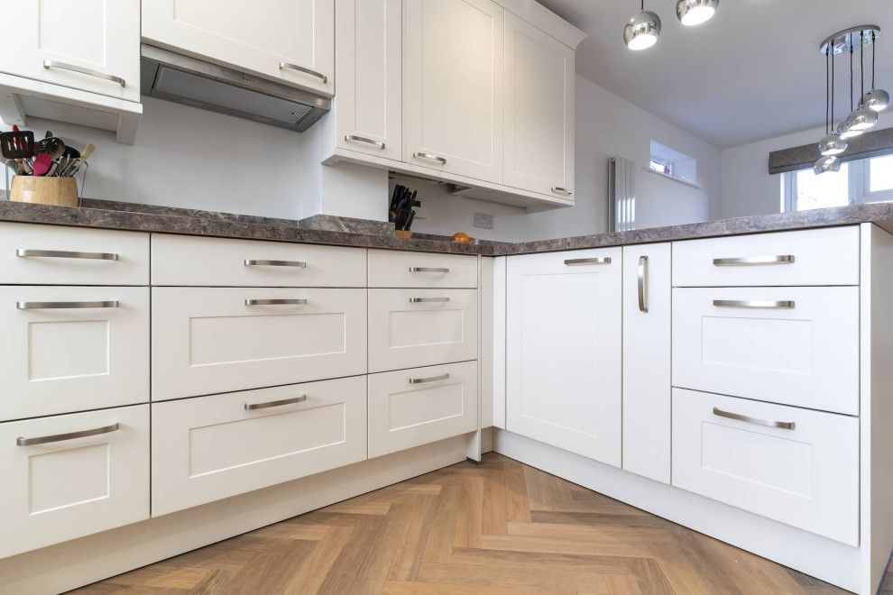 Photo of a small classic u-shaped kitchen in Oxfordshire with a submerged sink, shaker cabinets, white cabinets, laminate countertops, black appliances, a breakfast bar and multicoloured worktops.