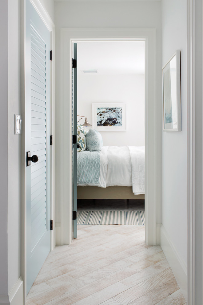 This is an example of a large beach style guest bedroom in Miami with white walls and light hardwood floors.