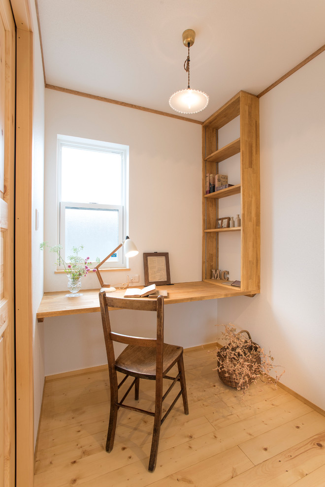Small asian home office in Other with white walls, light hardwood floors, a built-in desk and brown floor.