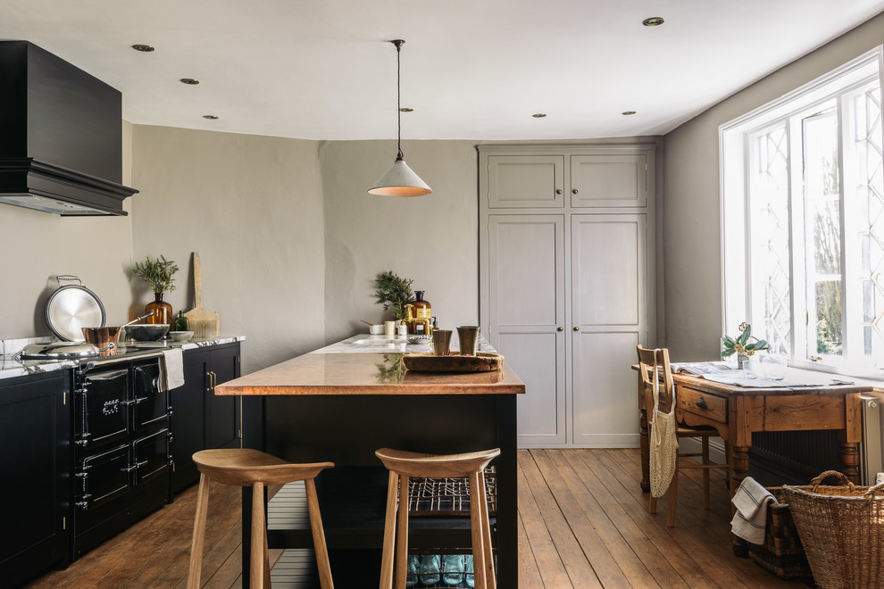 Inspiration for a mid-sized country single-wall open plan kitchen in Other with an integrated sink, shaker cabinets, black cabinets, copper benchtops, grey splashback, black appliances, medium hardwood floors and with island.