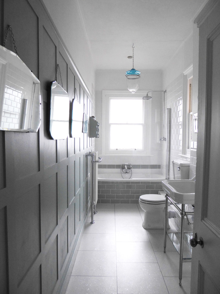 Inspiration for a mid-sized traditional bathroom in Sussex with recessed-panel cabinets, white cabinets, a drop-in tub, a shower/bathtub combo, a two-piece toilet, white tile, ceramic tile, green walls, laminate floors, white floor, a hinged shower door and a console sink.