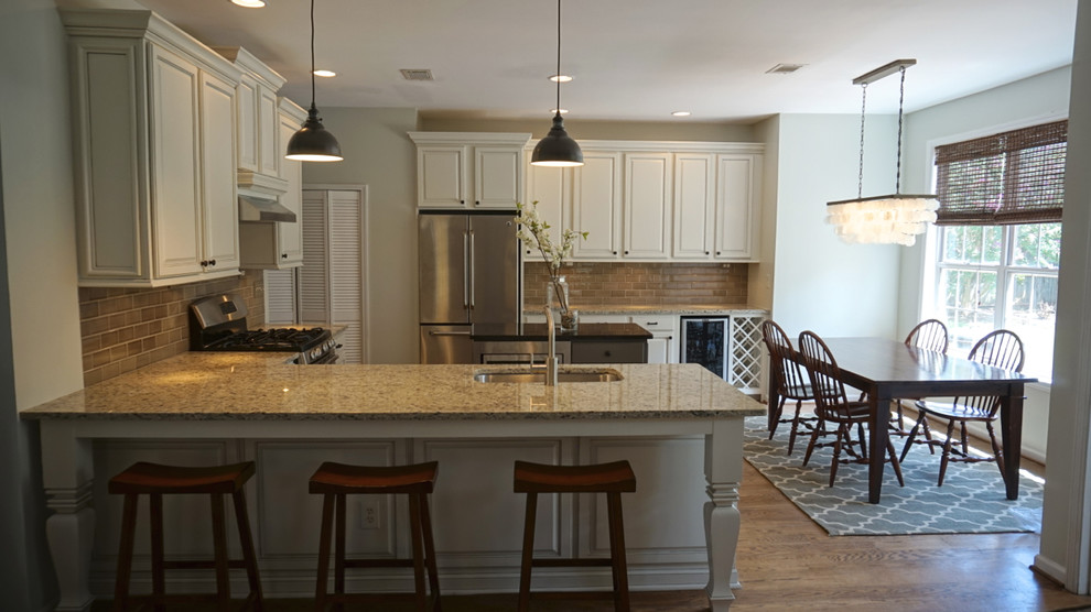 Inspiration for a large transitional u-shaped medium tone wood floor eat-in kitchen remodel in Atlanta with an undermount sink, raised-panel cabinets, white cabinets, granite countertops, gray backsplash, ceramic backsplash, stainless steel appliances and an island