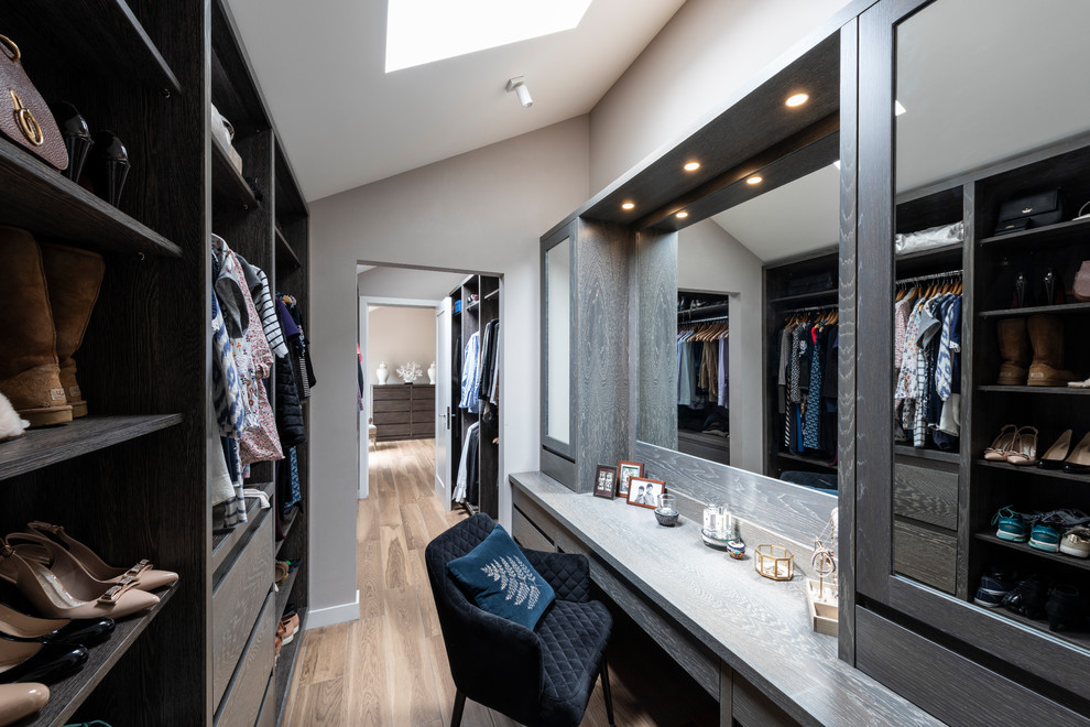 Design ideas for a mid-sized transitional women's dressing room in London with flat-panel cabinets, dark wood cabinets, light hardwood floors and brown floor.