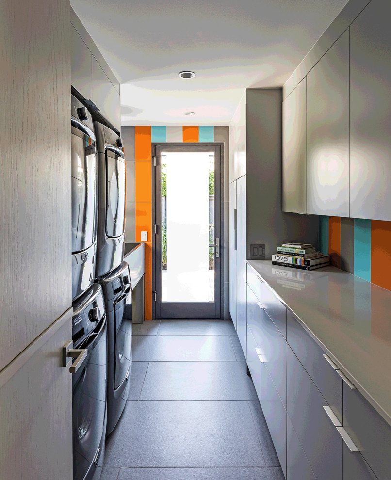 Inspiration for a small contemporary galley dedicated laundry room in Dallas with an utility sink, flat-panel cabinets, grey cabinets, quartz benchtops, orange walls, ceramic floors, a stacked washer and dryer, grey floor and grey benchtop.