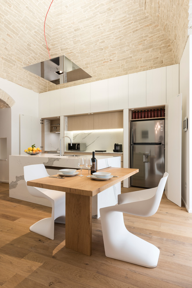 Large mediterranean galley eat-in kitchen in Bari with flat-panel cabinets, white cabinets, white splashback, stainless steel appliances, medium hardwood floors, brown floor, an undermount sink, with island and white benchtop.