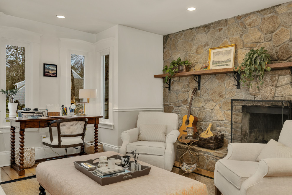 Mid-sized country study room in Boston with beige walls, light hardwood floors, a standard fireplace, a stone fireplace surround, a freestanding desk and brown floor.