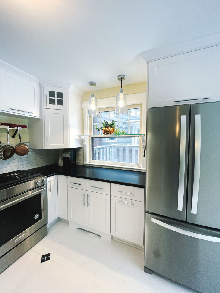 Example of a mid-sized ceramic tile and white floor kitchen design with an undermount sink, white cabinets, quartzite countertops, white backsplash, ceramic backsplash, stainless steel appliances, no island and black countertops