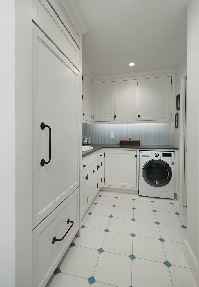 Inspiration for a transitional laundry room in Oklahoma City with a farmhouse sink, shaker cabinets, white cabinets, solid surface benchtops, blue walls, limestone floors, an integrated washer and dryer, white floor and grey benchtop.