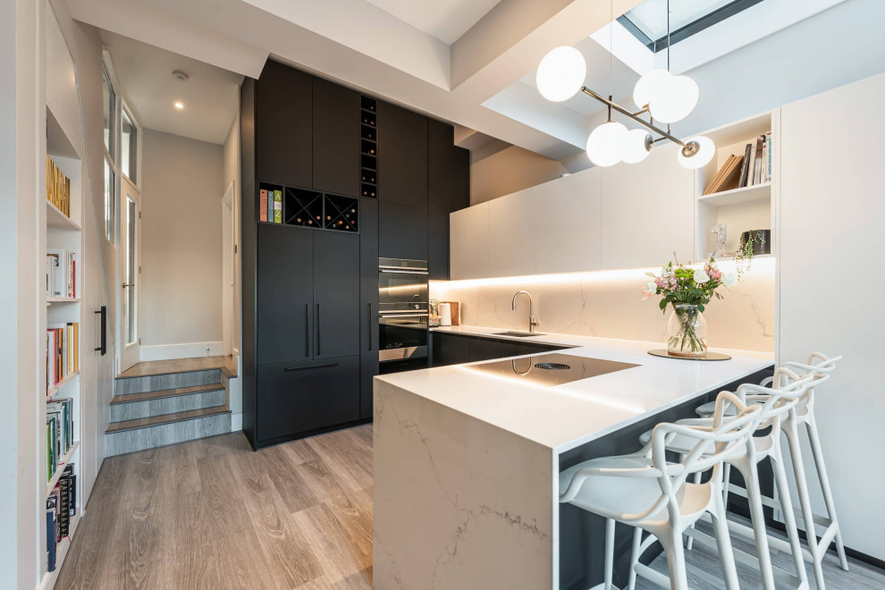 Design ideas for a small contemporary u-shaped open plan kitchen in London with a submerged sink, black cabinets, quartz worktops, engineered quartz splashback, black appliances, light hardwood flooring, grey floors, white worktops, a coffered ceiling, feature lighting, flat-panel cabinets, white splashback and a breakfast bar.