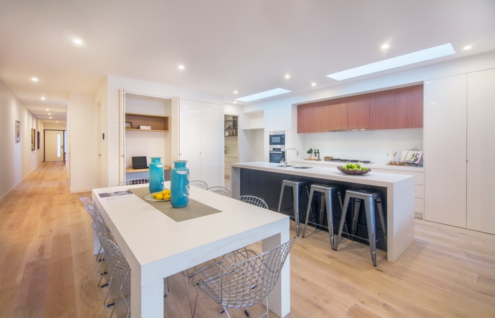 This is an example of a mid-sized contemporary galley eat-in kitchen in Melbourne with an undermount sink, flat-panel cabinets, quartz benchtops, white splashback, stainless steel appliances, light hardwood floors and with island.