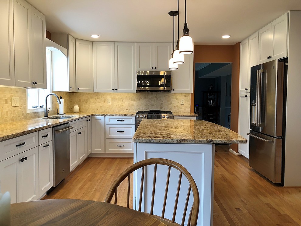 This is an example of a large transitional l-shaped eat-in kitchen in Baltimore with an undermount sink, shaker cabinets, white cabinets, granite benchtops, beige splashback, travertine splashback, stainless steel appliances, light hardwood floors, with island, beige floor and beige benchtop.