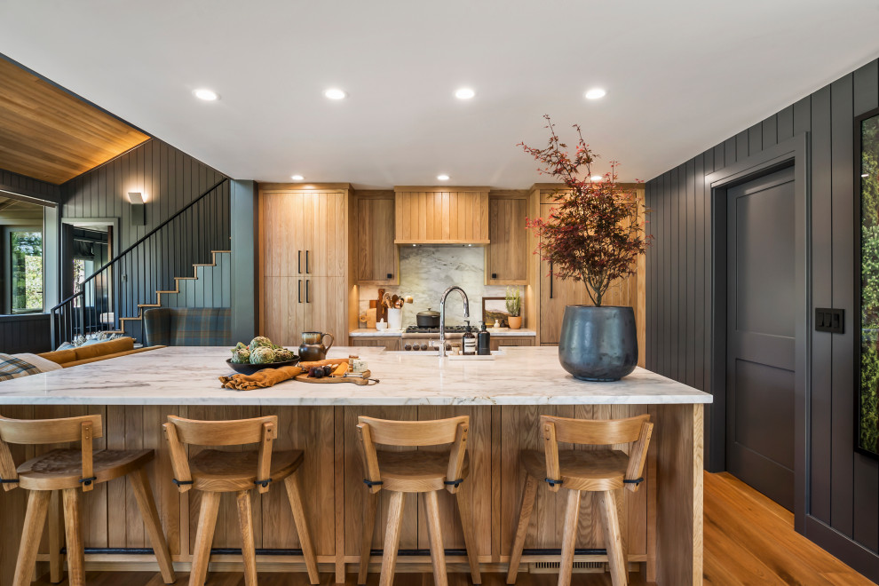 Example of a mountain style galley medium tone wood floor, brown floor and shiplap ceiling kitchen design with a farmhouse sink, flat-panel cabinets, medium tone wood cabinets, white backsplash, stone slab backsplash, paneled appliances, an island and white countertops