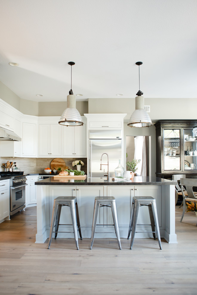 Open concept kitchen - large transitional l-shaped light wood floor open concept kitchen idea in Orange County with a farmhouse sink, beaded inset cabinets, white cabinets, beige backsplash, stone tile backsplash, stainless steel appliances, gray walls and an island