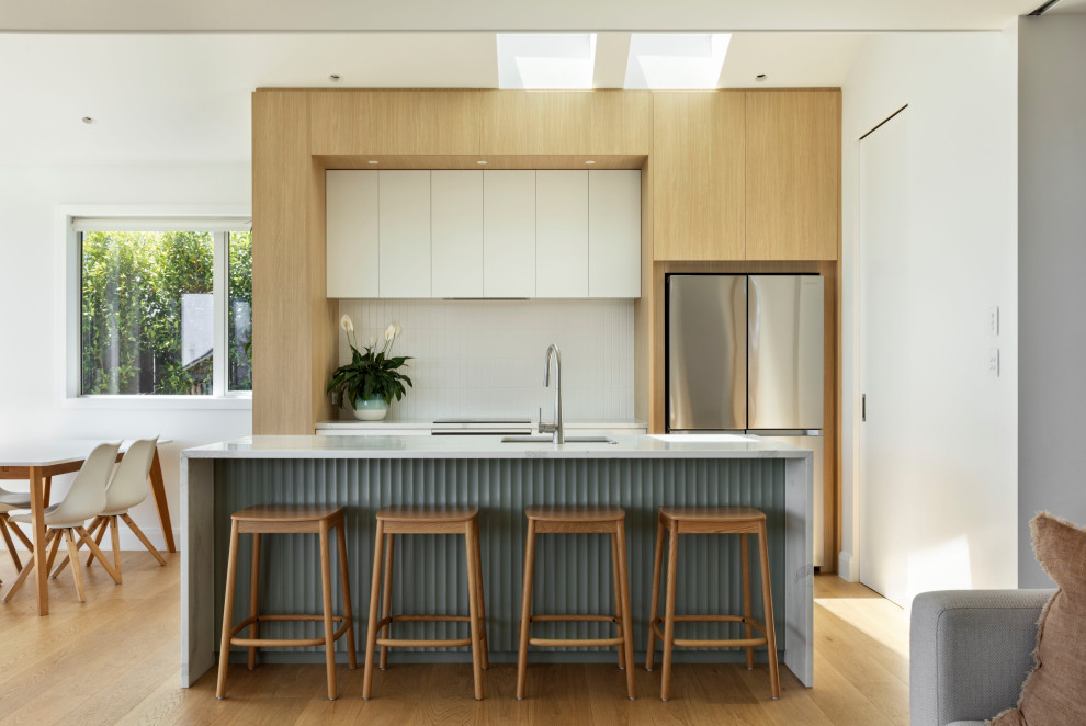 Design ideas for a Mid-sized contemporary Galley open plan kitchen in Auckland With Quartz Benchtops, White Splashback, with Island, an Undermount Sink, Flat-panel Cabinets, Light Wood Cabinets, Stainless Steel Appliances, Light Hardwood Floors, Beige Floor and White Benchtop.