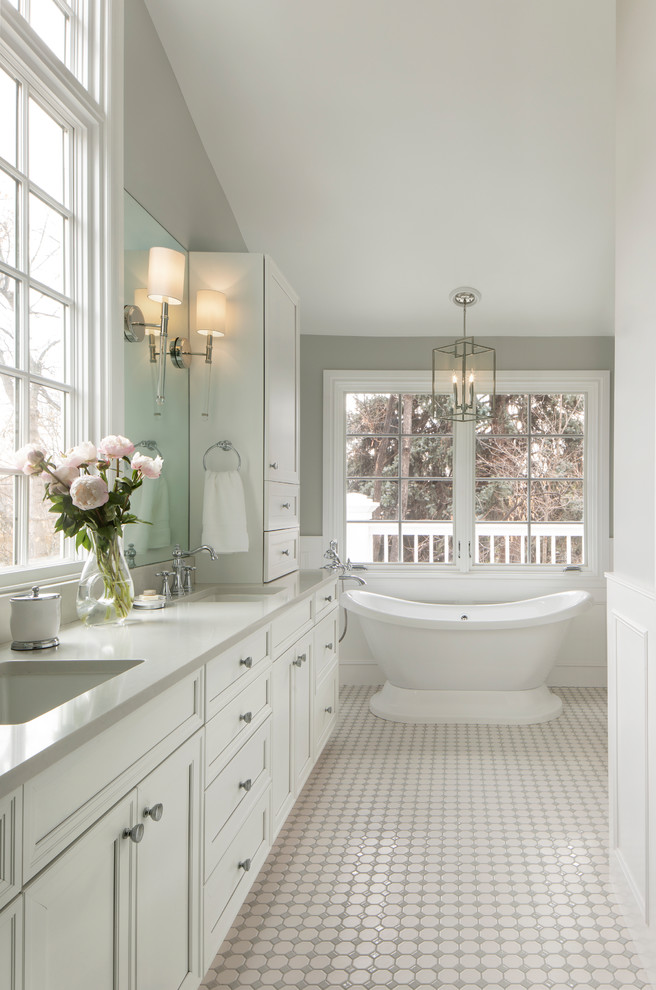 This is an example of a traditional bathroom in Denver with recessed-panel cabinets, white cabinets, a freestanding tub, grey walls, mosaic tile floors, an undermount sink, white floor and grey benchtops.