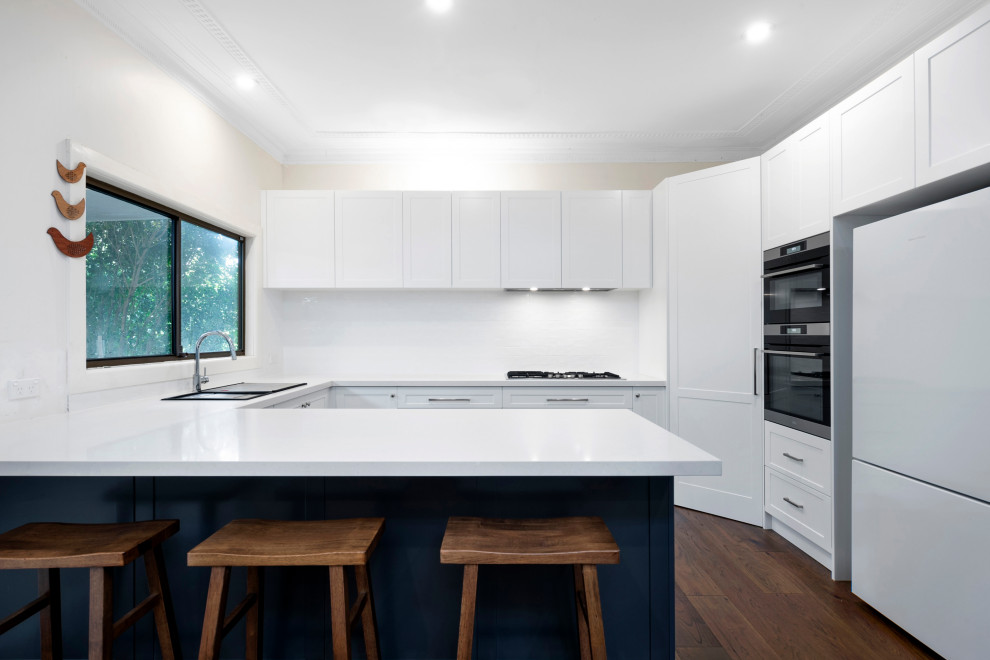 Photo of a mid-sized contemporary u-shaped kitchen pantry in Sydney with shaker cabinets, white cabinets, white splashback, ceramic splashback, a peninsula and white benchtop.