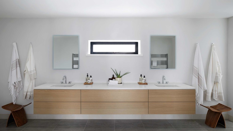 This is an example of a large modern master bathroom in London with flat-panel cabinets, light wood cabinets, a freestanding tub, an open shower, a one-piece toilet, beige tile, porcelain tile, grey walls, porcelain floors, an integrated sink, engineered quartz benchtops, grey floor, a hinged shower door and white benchtops.