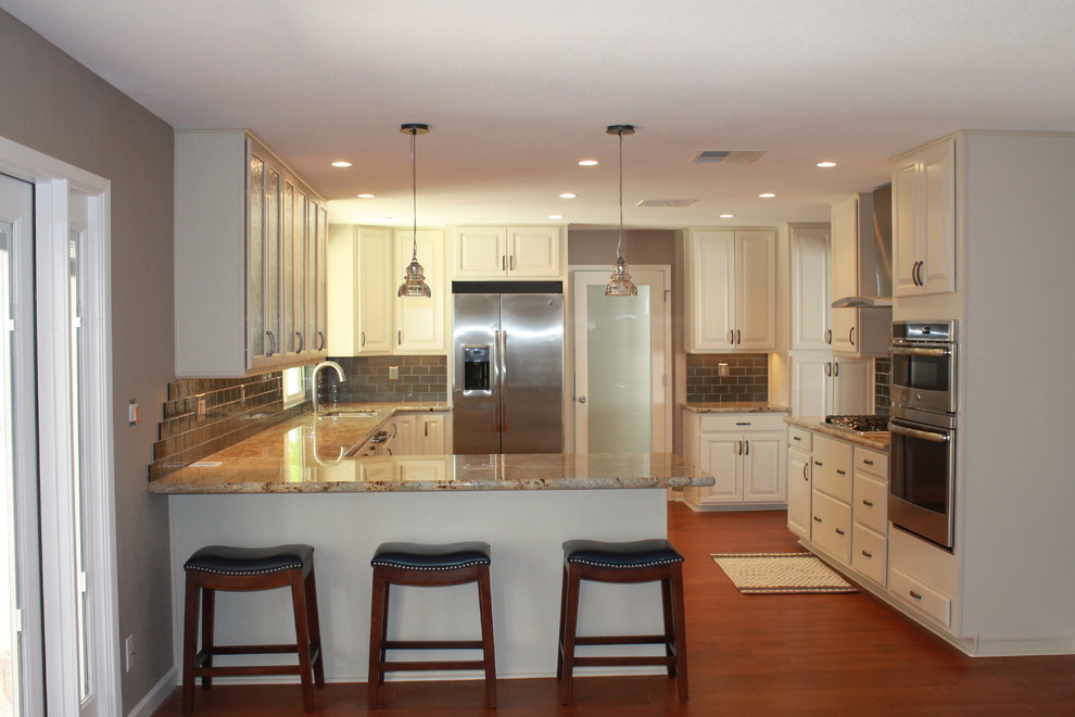 Inspiration for a mid-sized transitional u-shaped dark wood floor and brown floor eat-in kitchen remodel in Phoenix with an undermount sink, raised-panel cabinets, white cabinets, granite countertops, green backsplash, glass tile backsplash, stainless steel appliances and a peninsula