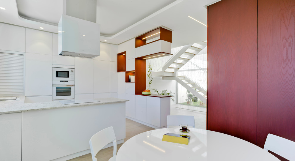 Inspiration for a large contemporary l-shaped open plan kitchen in Other with a single-bowl sink, flat-panel cabinets, white cabinets, light hardwood floors and a peninsula.