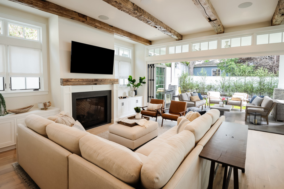 Imagen de sala de estar abierta de estilo de casa de campo grande con paredes beige, suelo de madera clara, marco de chimenea de piedra, pared multimedia, suelo marrón y vigas vistas