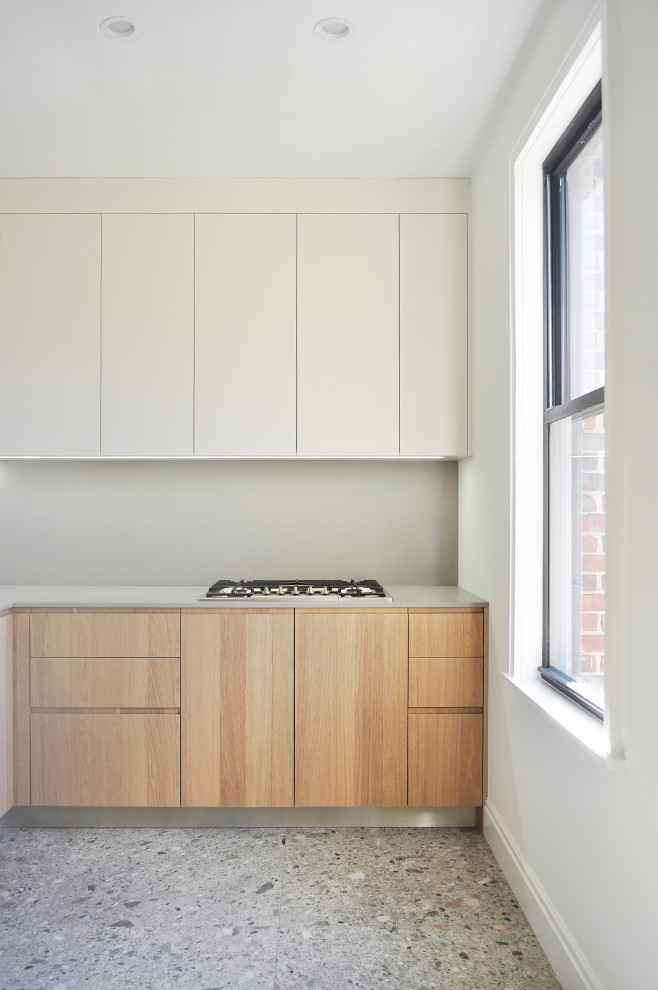 Inspiration for a small contemporary l-shaped separate kitchen in New York with an undermount sink, flat-panel cabinets, light wood cabinets, solid surface benchtops, grey splashback, stone slab splashback, stainless steel appliances, terrazzo floors, grey floor and grey benchtop.