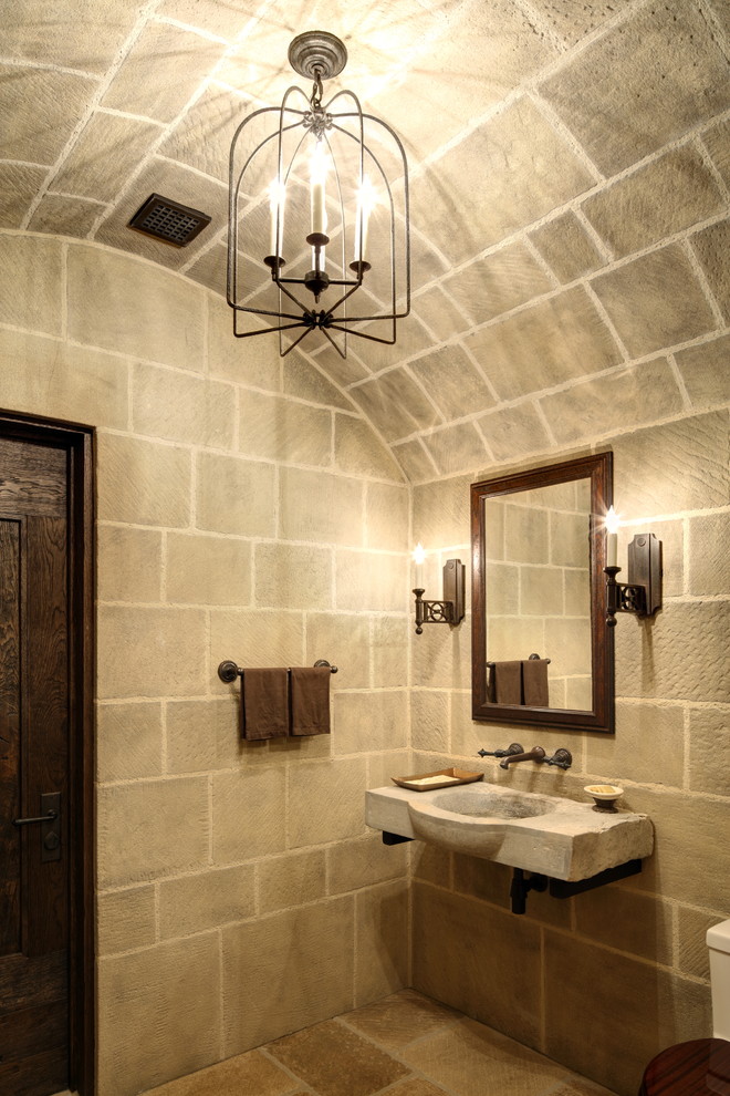 Design ideas for a mediterranean powder room in Other with beige tile, stone tile, beige walls, a wall-mount sink and beige floor.
