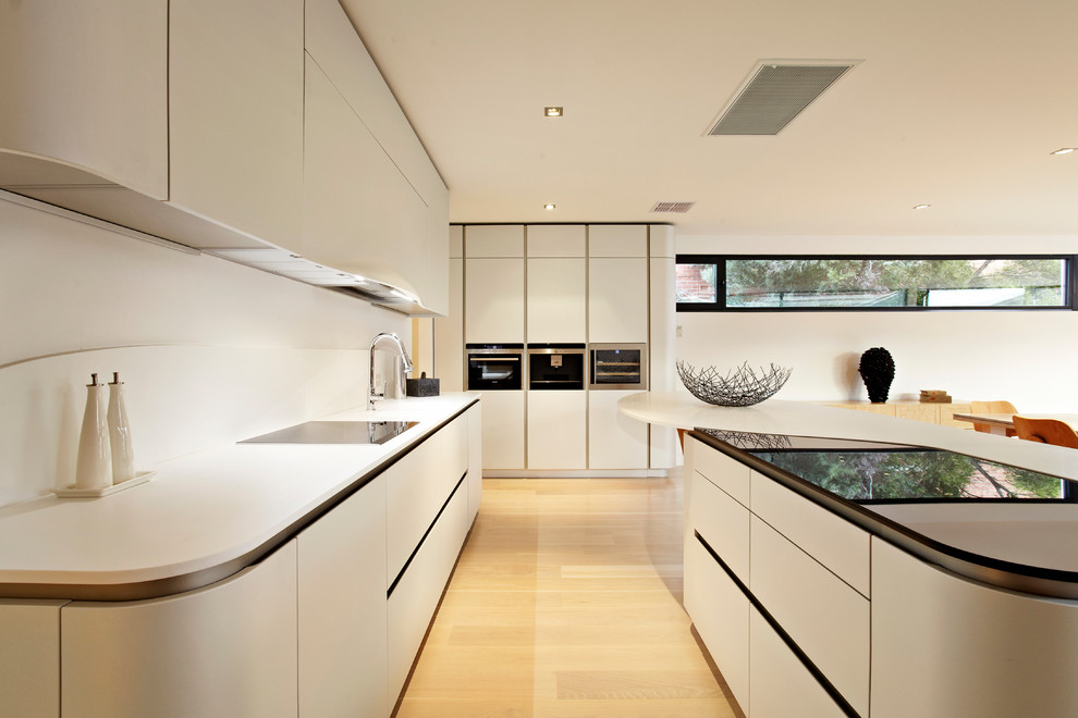 Contemporary galley eat-in kitchen in Melbourne with an integrated sink, flat-panel cabinets, white cabinets, solid surface benchtops, white splashback, stone slab splashback and black appliances.