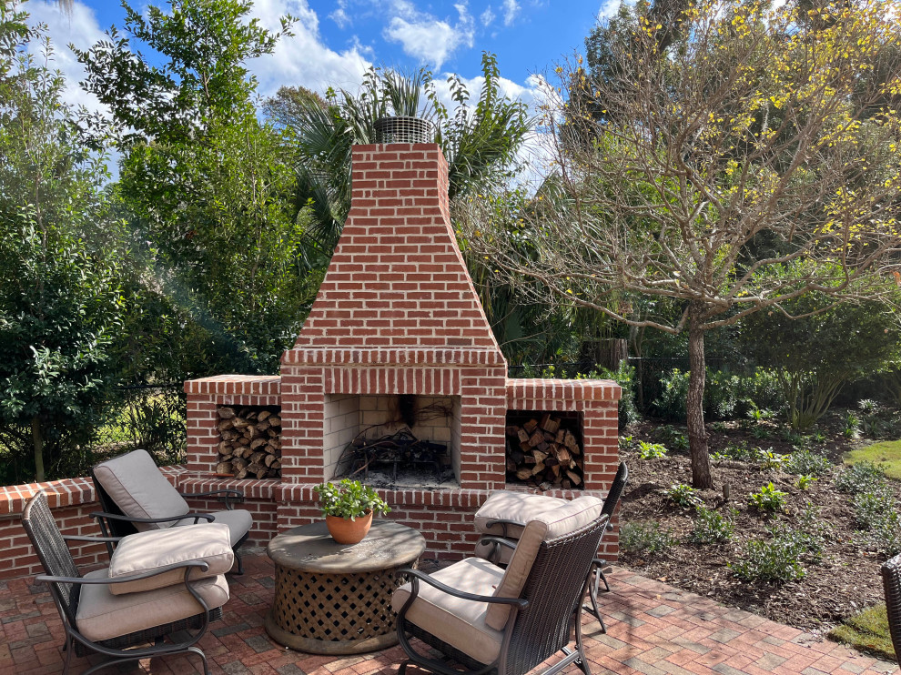 This is an example of a traditional backyard full sun garden in Jacksonville with with fireplace, brick pavers and a wood fence.
