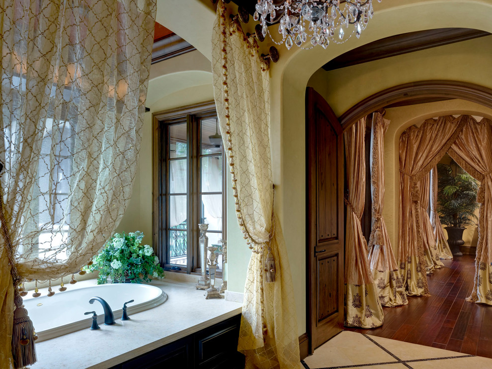 This is an example of a large mediterranean master bathroom in Orlando with raised-panel cabinets, dark wood cabinets, a drop-in tub, beige tile, travertine, green walls and travertine floors.