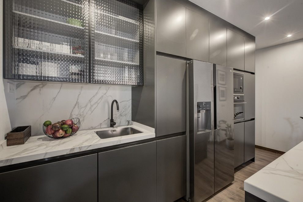 Photo of a mid-sized industrial open plan kitchen in Madrid with a single-bowl sink, glass-front cabinets, grey cabinets, marble benchtops, panelled appliances, laminate floors, with island and brown floor.