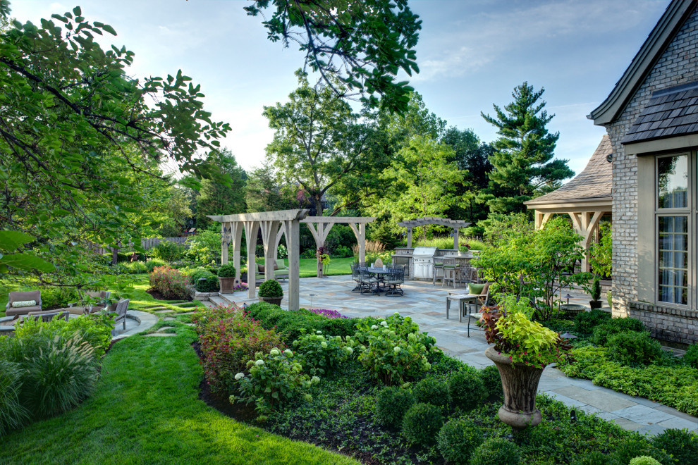 Modelo de jardín clásico renovado grande en verano en patio trasero con brasero, exposición parcial al sol y adoquines de piedra natural