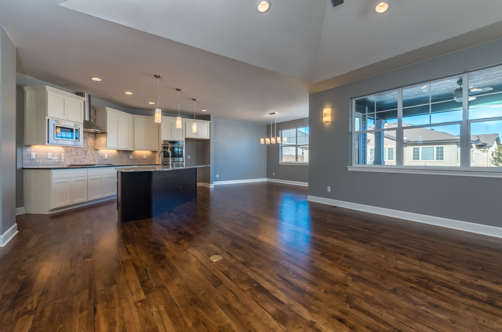 Open concept kitchen - transitional l-shaped medium tone wood floor open concept kitchen idea in Denver with an undermount sink, recessed-panel cabinets, dark wood cabinets, granite countertops, beige backsplash, stone tile backsplash, stainless steel appliances and an island