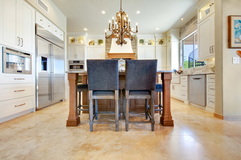 Inspiration for a large transitional u-shaped travertine floor and beige floor open concept kitchen remodel in Phoenix with a farmhouse sink, recessed-panel cabinets, white cabinets, granite countertops, gray backsplash, porcelain backsplash, stainless steel appliances, an island and multicolored countertops