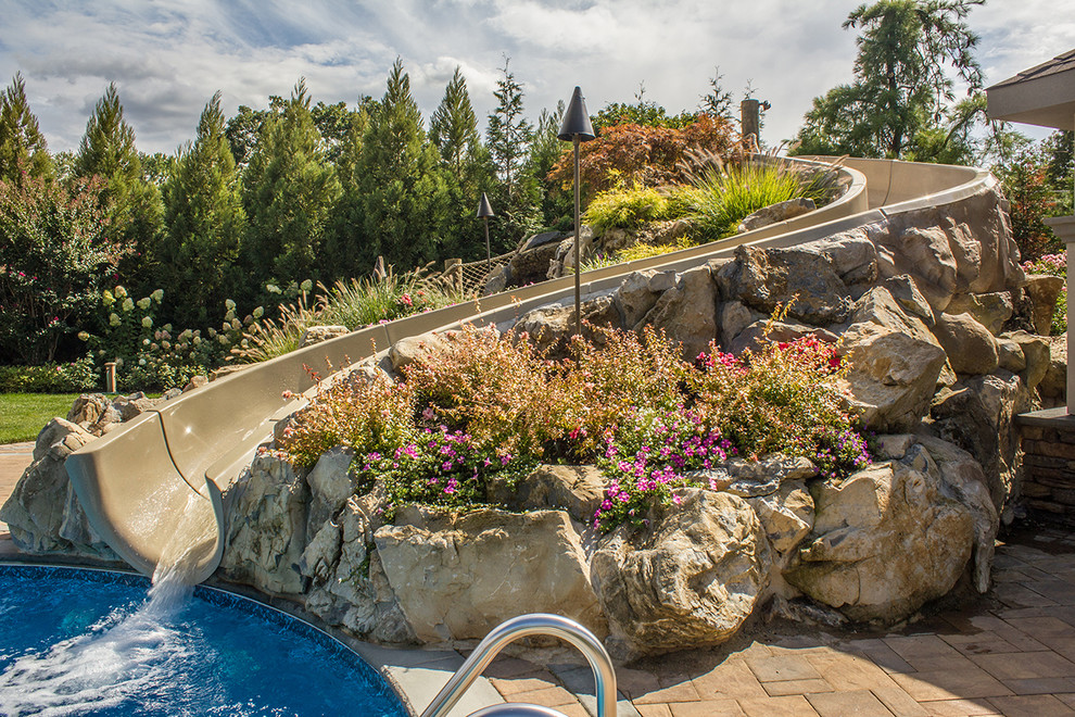 This is an example of a large beach style backyard custom-shaped natural pool in New York with a water slide and concrete pavers.